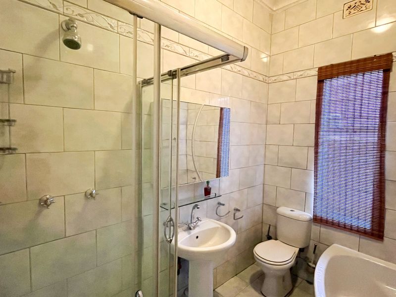 A functional bathroom featuring a shower enclosure, pedestal basin, toilet, and neutral wall tiling throughout.