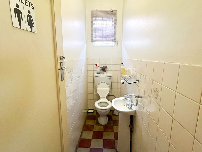 A compact guest bathroom featuring a pedestal basin, toilet, and tiled finishes, presenting a dated aesthetic suitable for modernization.