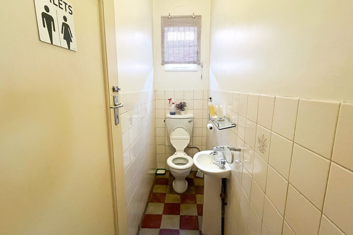 A compact guest bathroom featuring a pedestal basin, toilet, and tiled finishes, presenting a dated aesthetic suitable for modernization.