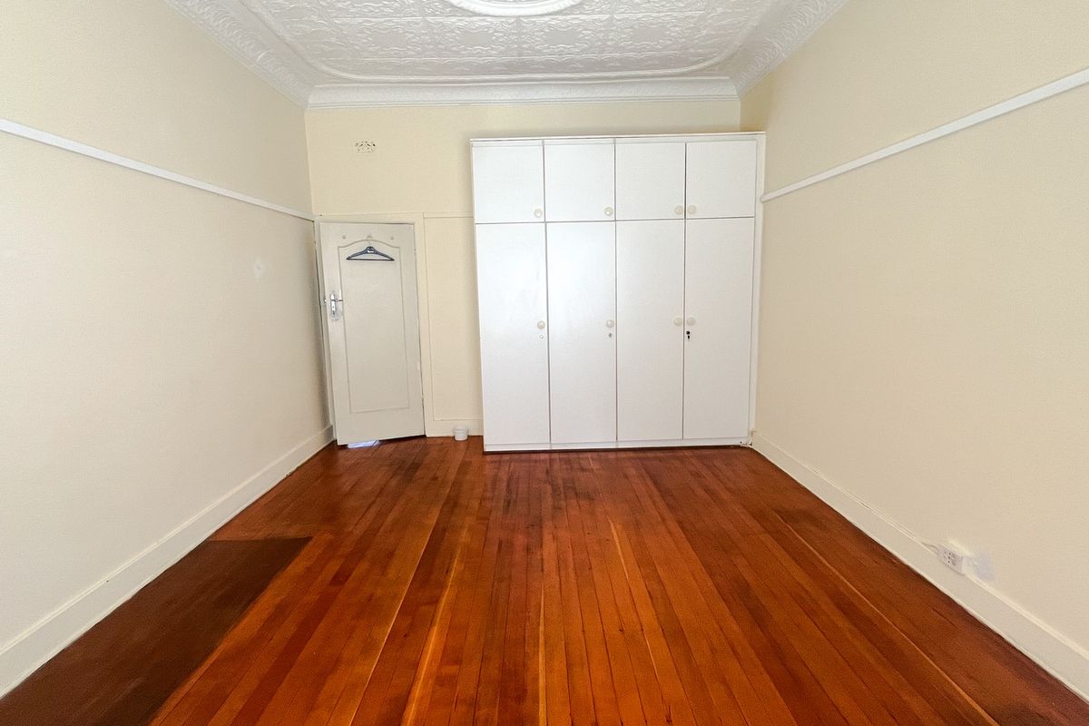 An empty bedroom featuring polished timber flooring, a built-in wardrobe, and an ornate ceiling rose with classic picture rail detailing.