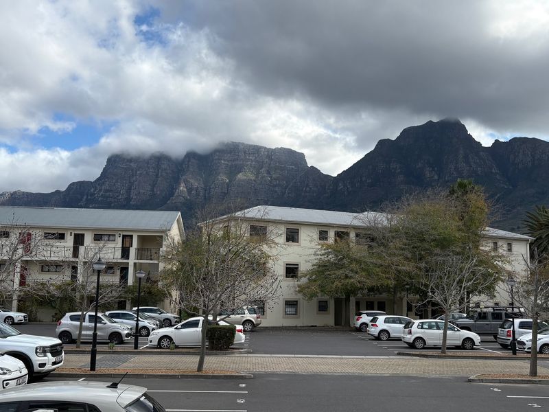 Exterior view of a multi-story apartment complex with a paved parking area and scenic mountain backdrop.