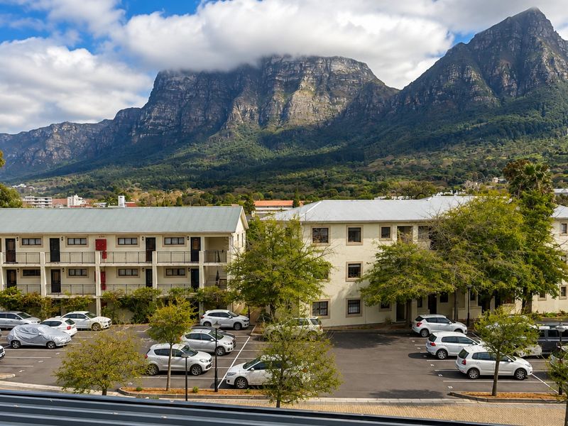 Exterior view of an apartment complex featuring a parking area, multi-story building structure, and scenic mountain backdrop.