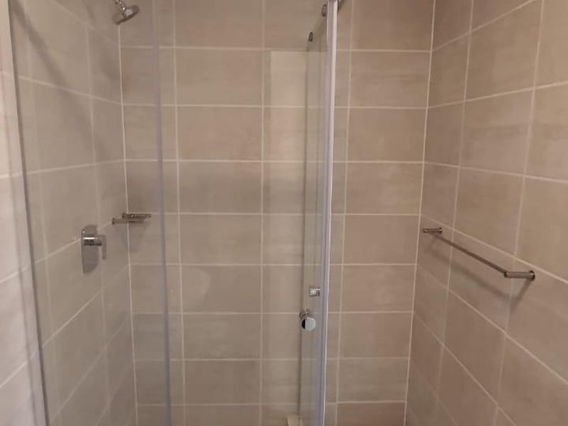 A clean, modern bathroom shower enclosure featuring neutral ceramic wall tiles, a glass door, and chrome fixtures.