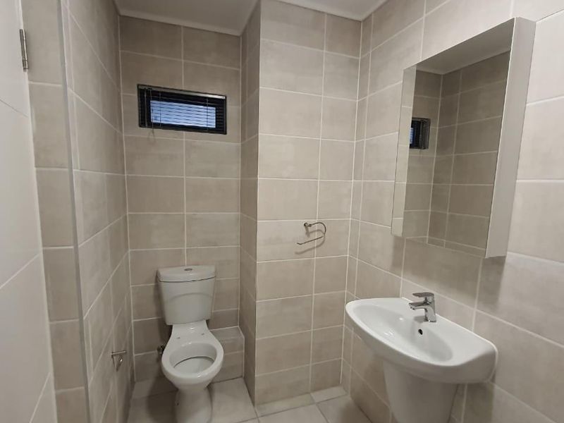 A clean, modern bathroom featuring neutral wall tiles, a pedestal basin, and a wall-mounted mirror.