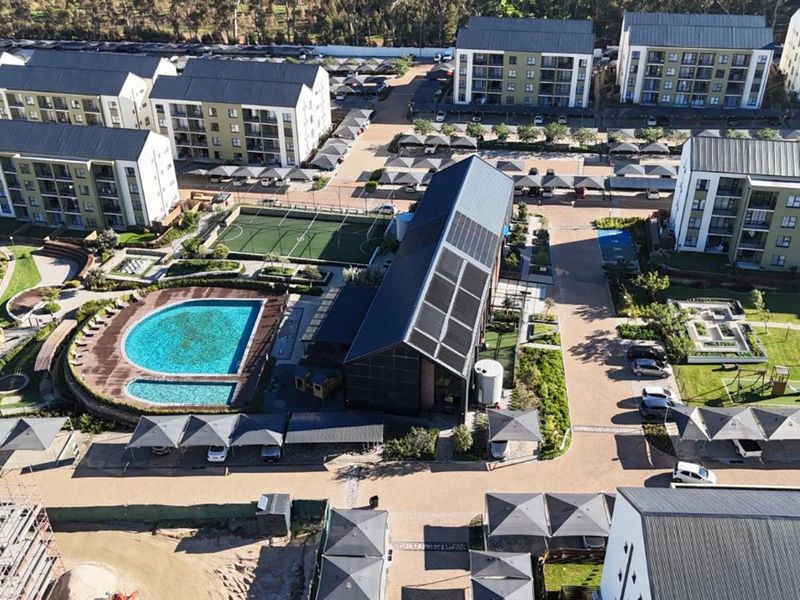 Aerial view of a modern apartment complex featuring a swimming pool, sports court, landscaped grounds, and extensive covered parking facilities.