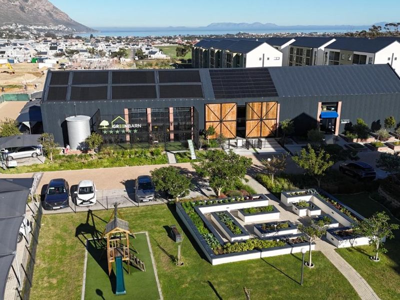 Aerial view of a modern industrial-style building featuring solar panels, raised garden beds, and landscaped grounds in a residential estate setting.