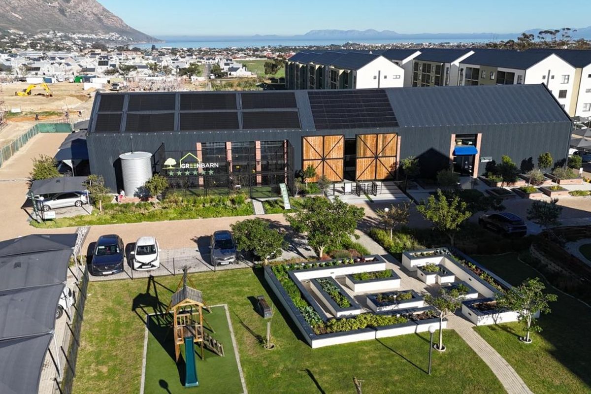 Aerial view of a modern industrial-style building featuring solar panels, raised garden beds, and landscaped grounds in a residential estate setting.