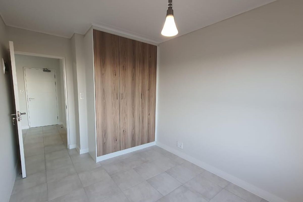 A clean, modern bedroom featuring neutral tiled flooring, built-in wood-finish cupboards, and a simple pendant light fixture.