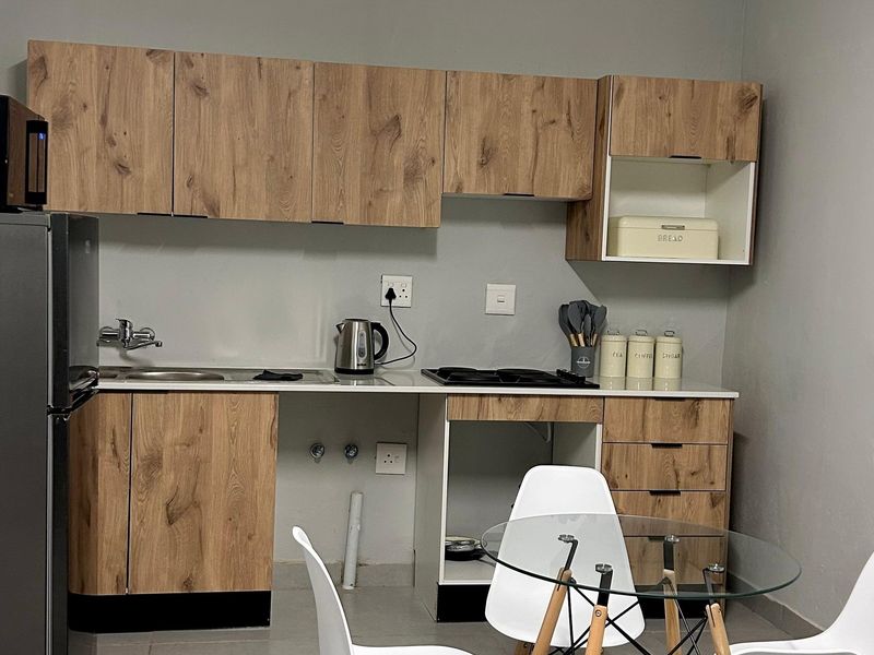 Compact kitchen featuring modern wood-look cabinetry, a built-in hob, and a stainless steel sink with a neutral countertop finish.