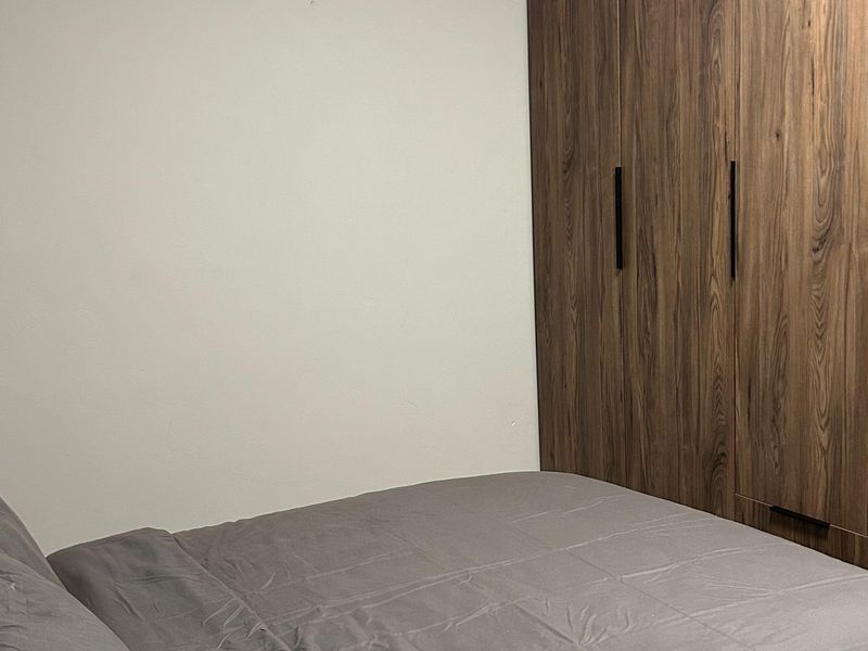 A bedroom featuring a modern, full-height built-in wardrobe with wood-grain finish and sleek black handles.