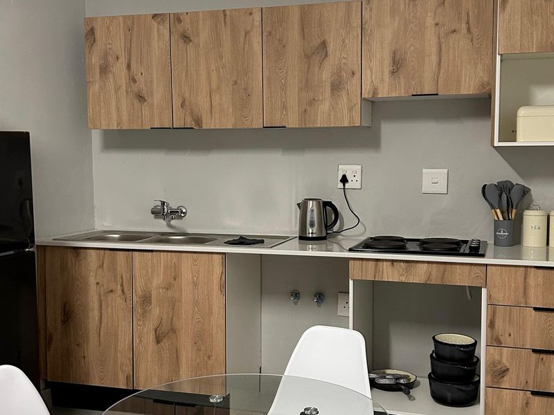 A compact kitchen featuring wood-look cabinetry, a double stainless steel sink, and a built-in electric hob with a clean, modern aesthetic.
