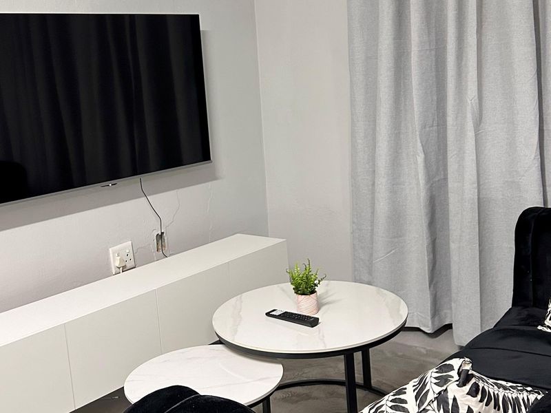 A living room area featuring a wall-mounted television, with visible wall cracks and unfinished electrical points requiring maintenance.