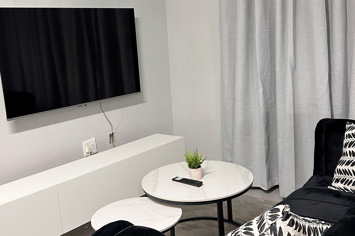 A living room area featuring a wall-mounted television, with visible wall cracks and unfinished electrical points requiring maintenance.