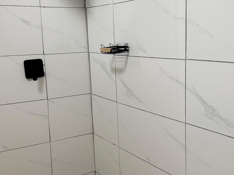 A clean, modern shower enclosure featuring white marble-look wall tiles and a minimalist black shower mixer.