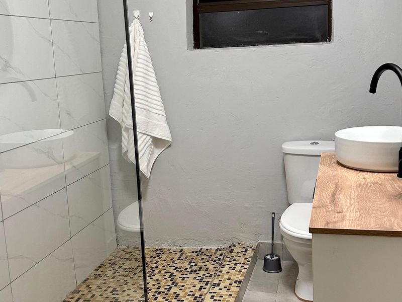 Modern bathroom featuring a glass-enclosed shower with mosaic tiling, a contemporary vanity with a vessel basin, and black fixtures.