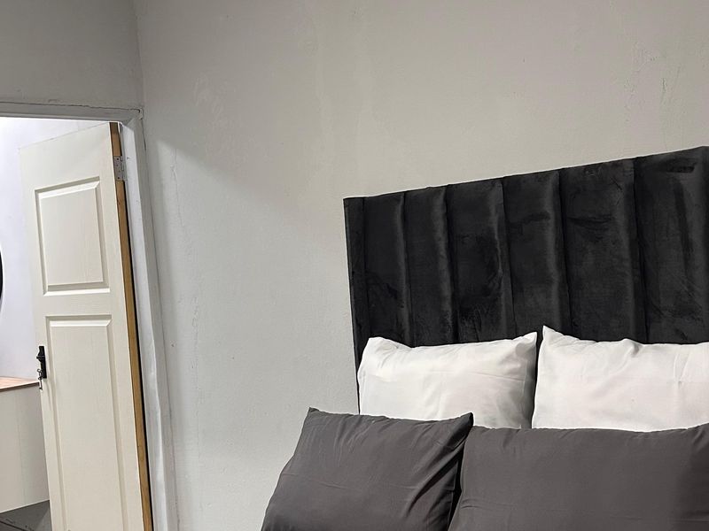 Bedroom featuring an en-suite bathroom with a modern vanity and mirror, showing visible wall plaster cracks requiring maintenance.