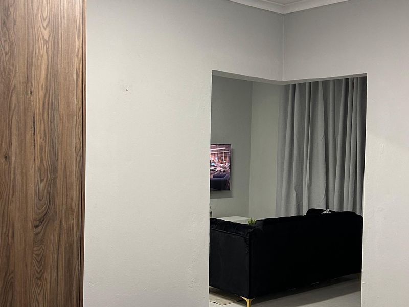 A bedroom interior featuring a modern wood-finish built-in wardrobe with a view into an adjacent living area.