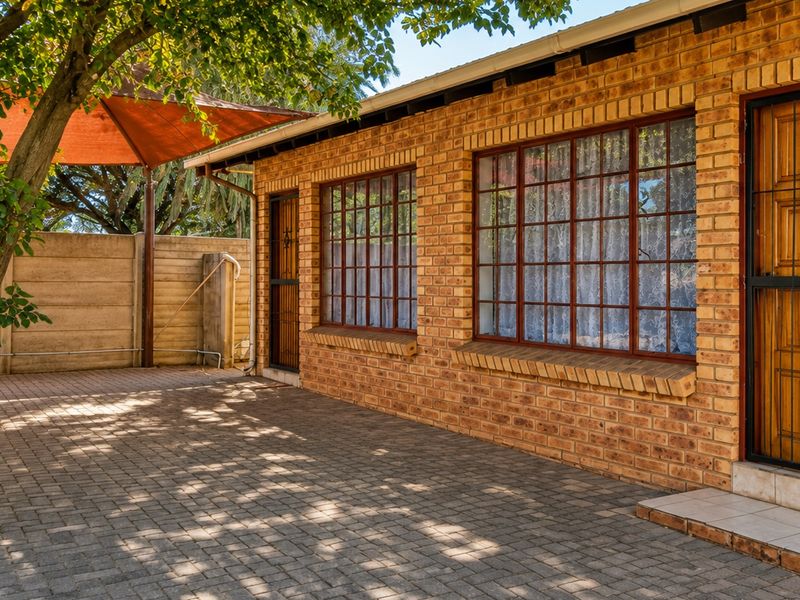 A well-maintained rear exterior featuring a face brick facade, paved patio area, and secure access points with security gates.