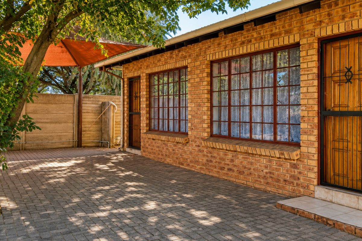 A well-maintained rear exterior featuring a face brick facade, paved patio area, and secure access points with security gates.
