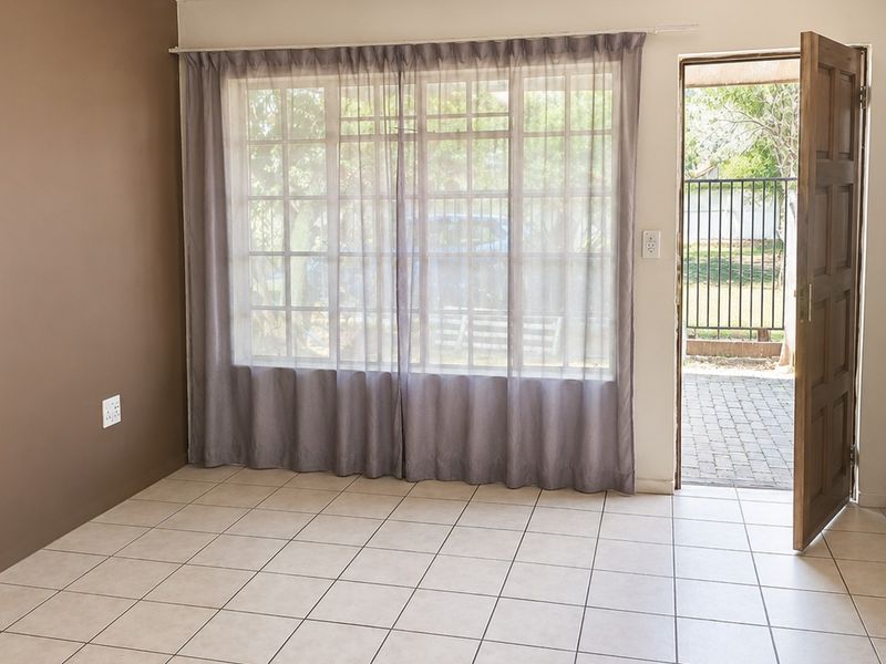 A bright, empty living area featuring tiled flooring, a large grid-pattern window, and direct access to an outdoor patio space.