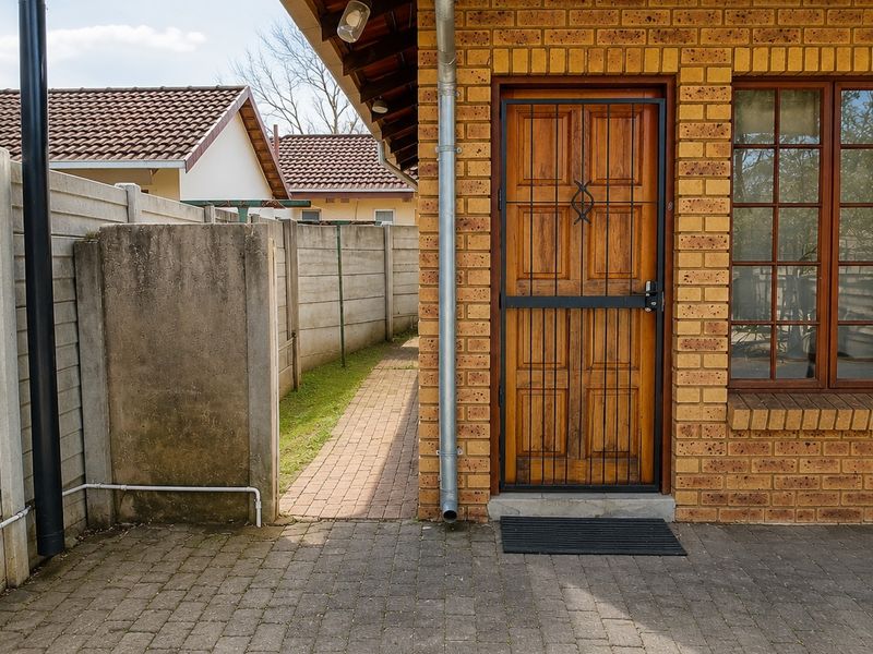 Rear exterior view of the property featuring a face brick facade, timber door with security gate, and a paved patio area.