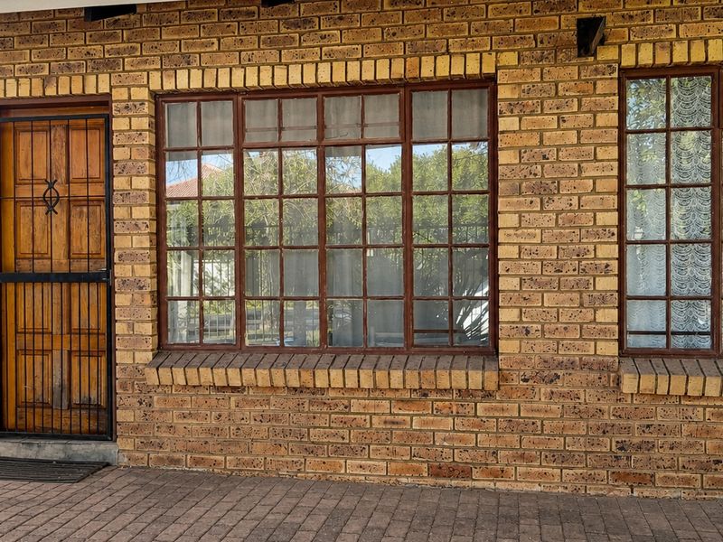 Front facade of the flat featuring face brick construction, timber-framed windows, and a secure entrance door with a metal security gate.
