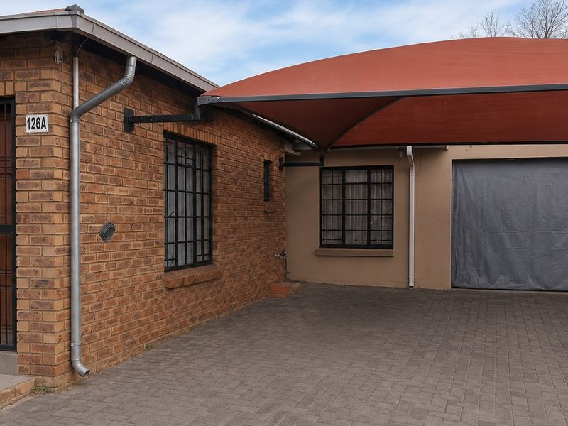 Front exterior view of the property featuring a brick facade, secure entrance, paved driveway, and a covered carport area.