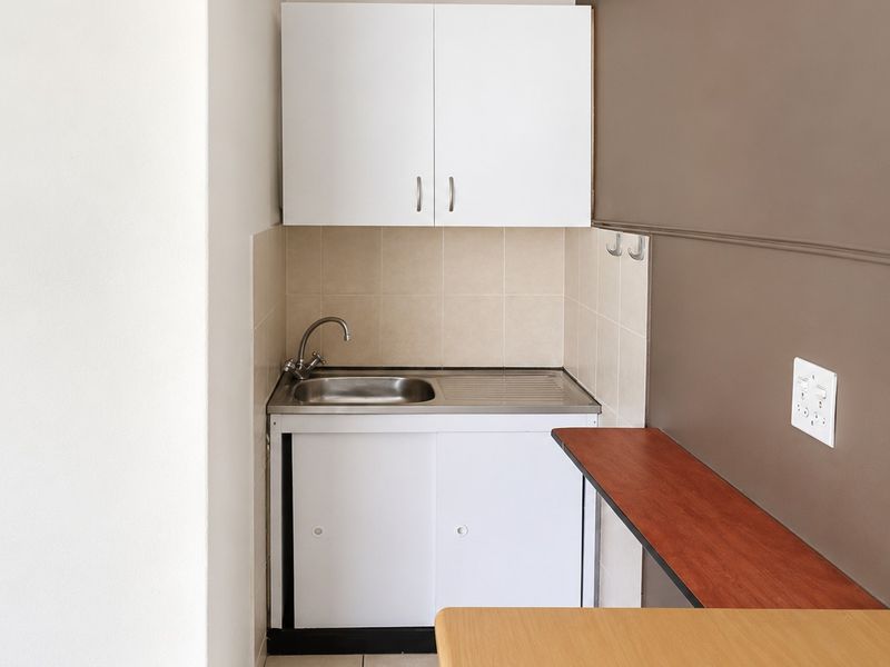 A compact kitchenette featuring a stainless steel sink, built-in white cabinetry, tiled splashback, and a functional wall-mounted shelf.