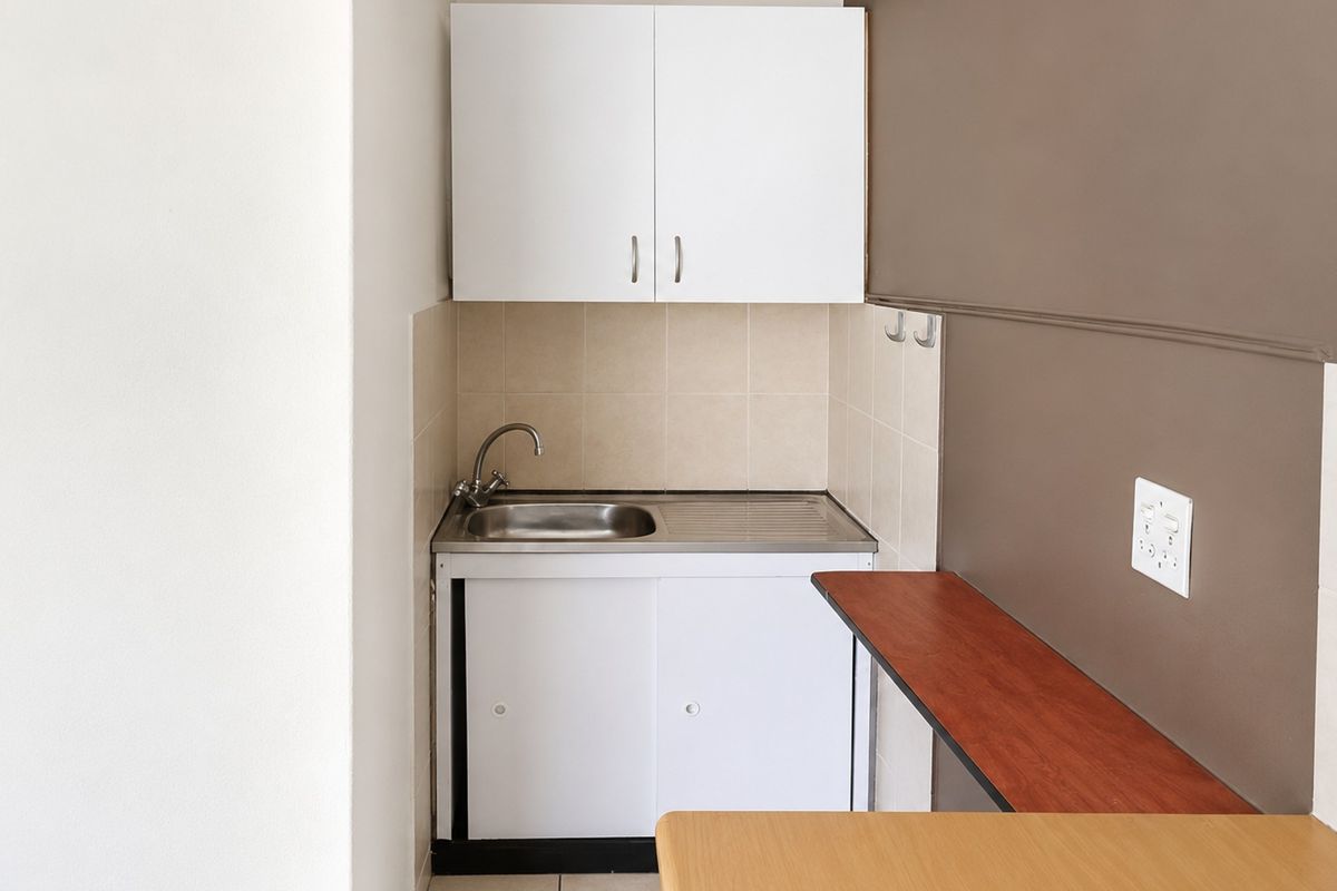 A compact kitchenette featuring a stainless steel sink, built-in white cabinetry, tiled splashback, and a functional wall-mounted shelf.