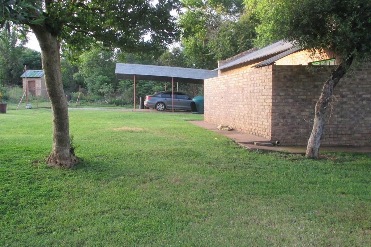 A view of the rear exterior featuring a brick building, a metal-roofed carport, and a spacious grass lawn.