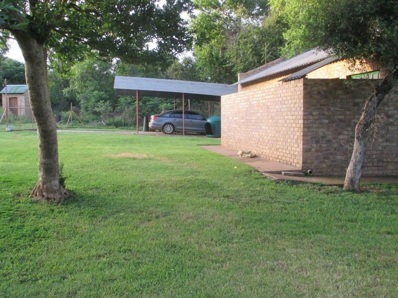 A view of the rear exterior featuring a brick building, a metal-roofed carport, and a spacious grass lawn.