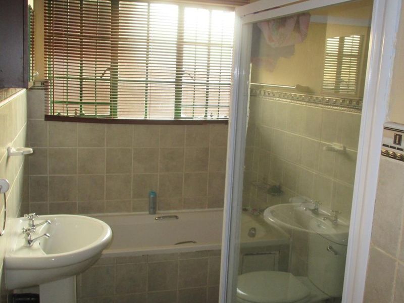 A functional bathroom featuring a pedestal basin, built-in bathtub, separate shower enclosure, and toilet with neutral wall tiling.