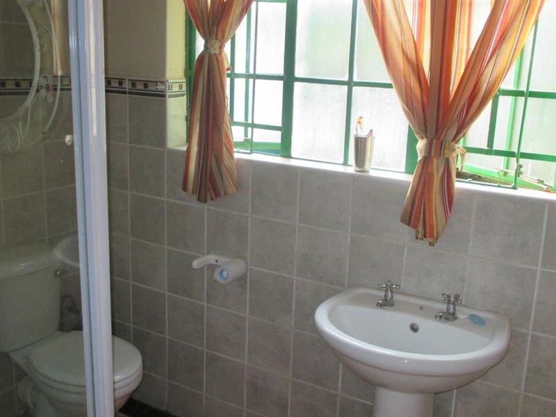 A functional bathroom featuring a pedestal basin, toilet, and tiled wall finishes with natural light from a window.