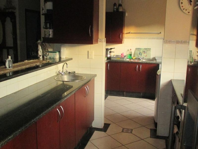 A functional kitchen featuring dark wood cabinetry, granite countertops, a stainless steel sink, and tiled flooring with a neutral backsplash.