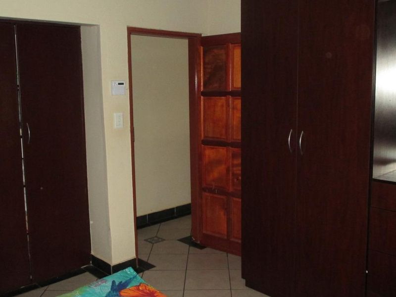 A bedroom featuring dark wood built-in cupboards, tiled flooring, and a wooden door leading to an adjacent space.