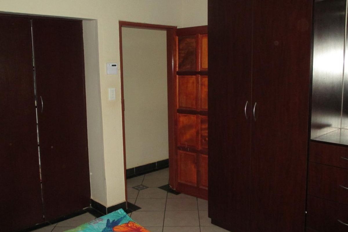 A bedroom featuring dark wood built-in cupboards, tiled flooring, and a wooden door leading to an adjacent space.