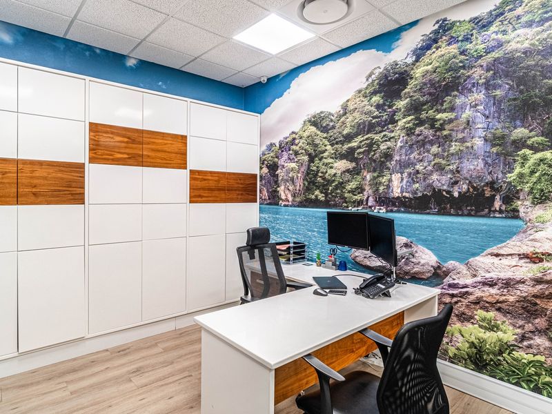A modern office space featuring extensive built-in storage cabinetry, a suspended ceiling with recessed lighting, and durable laminate flooring.