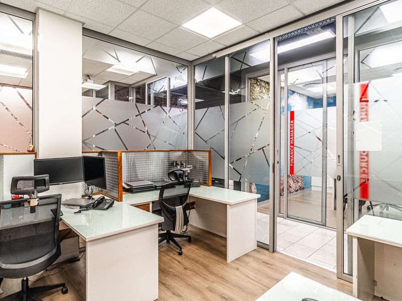 Modern office space featuring glass partition walls with frosted privacy film, suspended ceiling with recessed lighting, and durable laminate flooring.