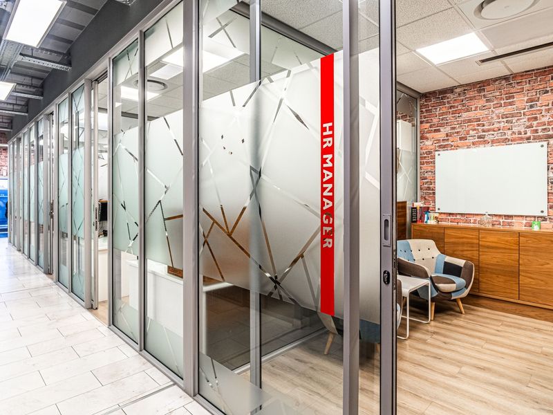 Modern office space featuring glass partition walls, exposed brick accents, and professional recessed lighting, creating a contemporary and functional workspace environment.