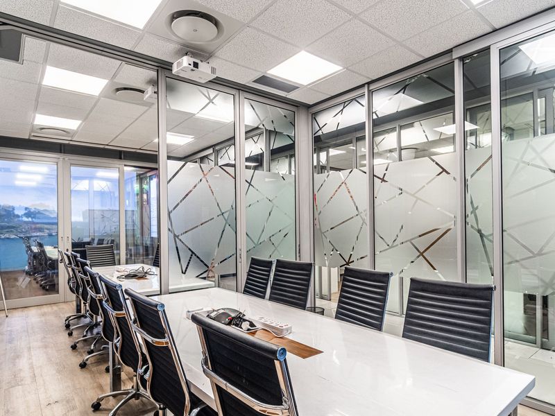 Modern professional boardroom featuring glass partition walls, suspended ceiling with recessed lighting, and integrated air conditioning, providing a bright and collaborative workspace.