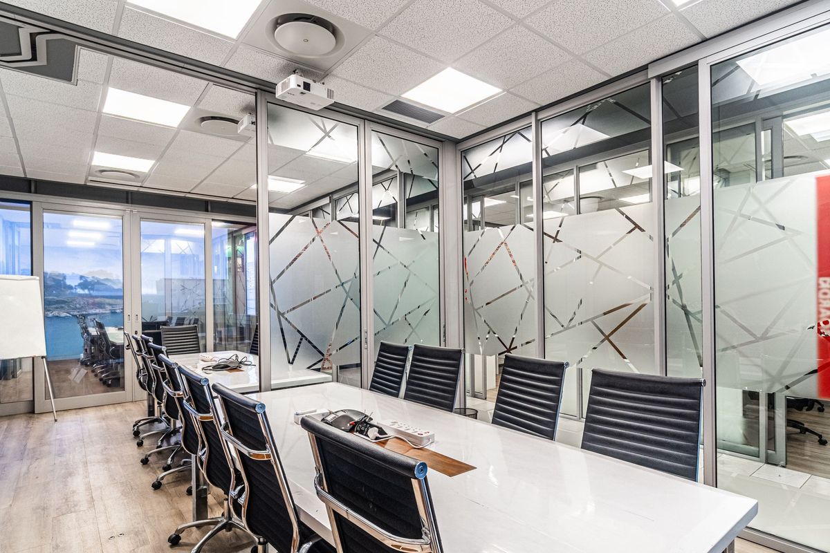 Modern professional boardroom featuring glass partition walls, suspended ceiling with recessed lighting, and integrated air conditioning, providing a bright and collaborative workspace.
