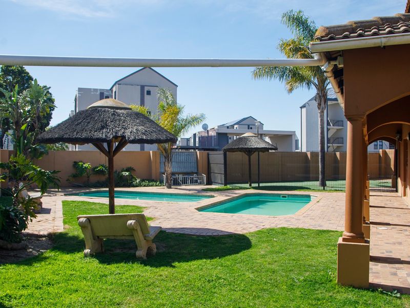 Outdoor pool area featuring two swimming pools, brick paving, thatched umbrellas, and a covered patio space within a secure complex.
