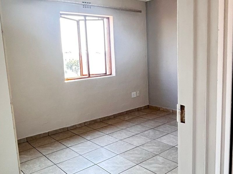 An empty bedroom featuring neutral tiled flooring and a window, providing a blank canvas for personalization.