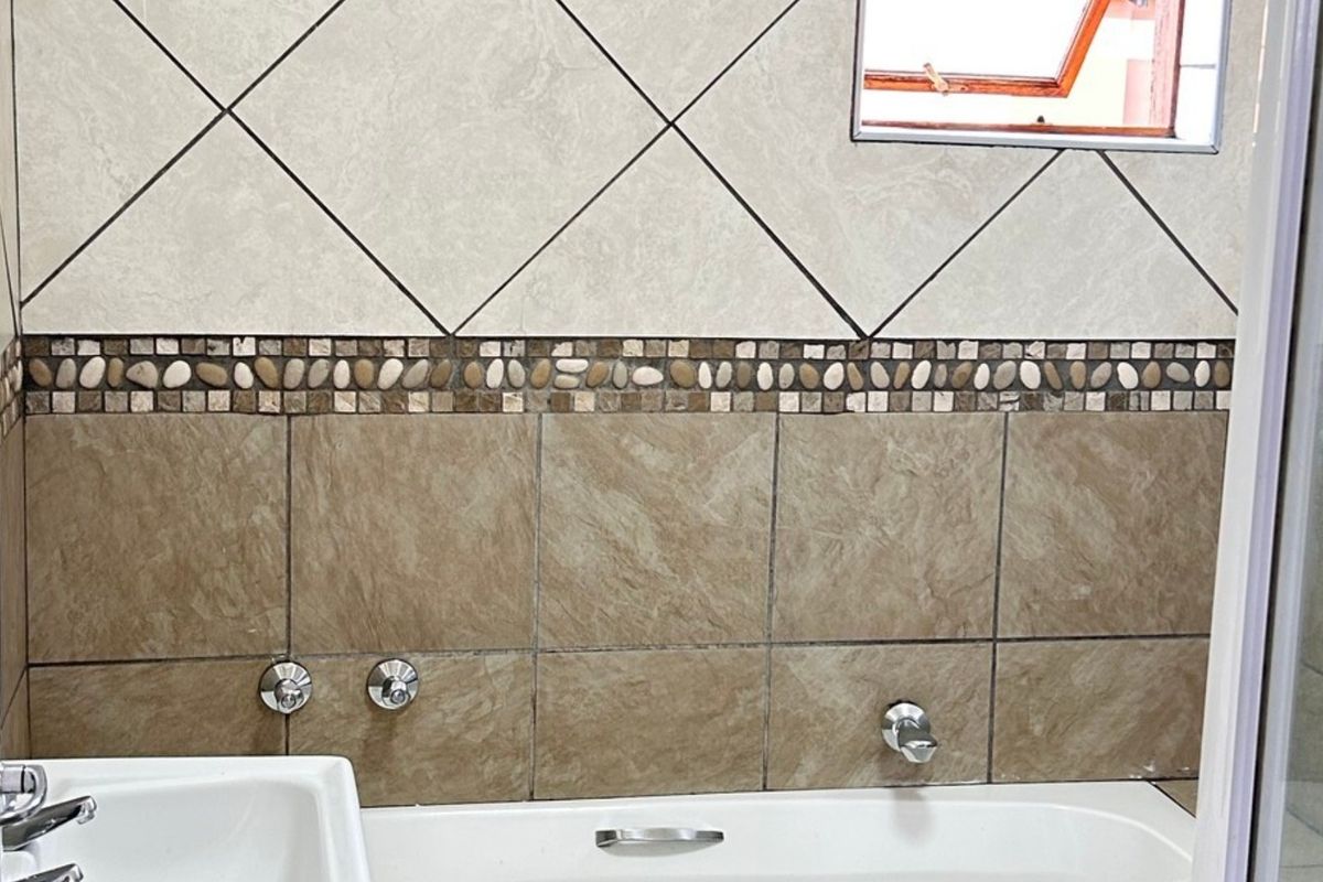 A bathroom featuring a built-in bathtub with chrome fixtures, decorative mosaic tile accents, and neutral wall tiling.