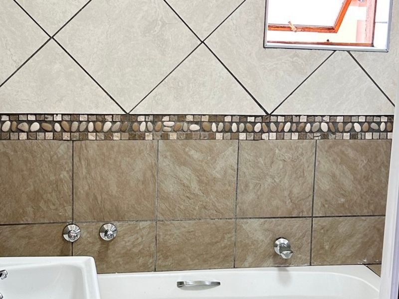 A bathroom featuring a built-in bathtub with chrome fixtures, decorative mosaic tile accents, and neutral wall tiling.