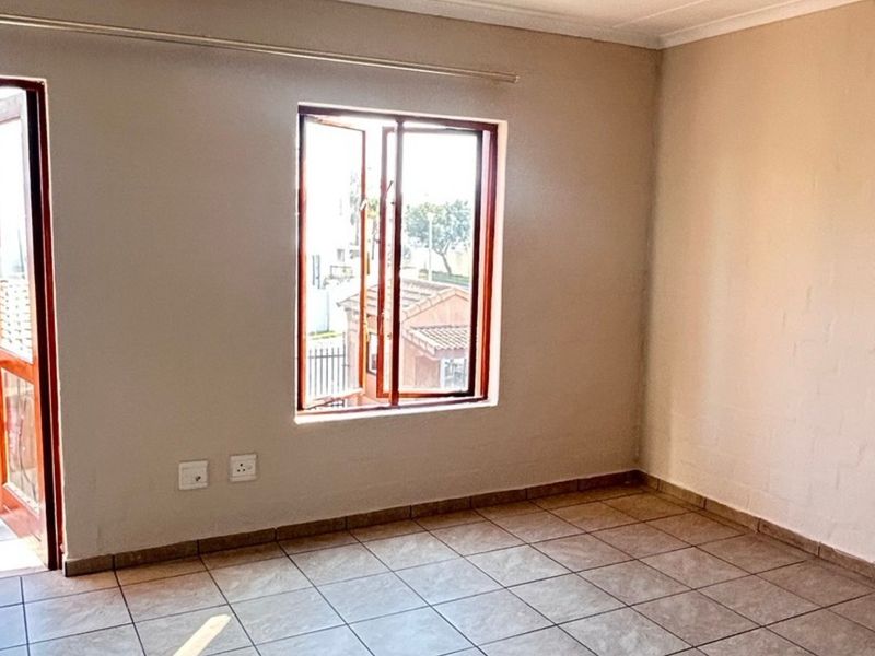 A bright, empty bedroom featuring tiled flooring, neutral walls, and a wooden window frame with access to an adjacent balcony.