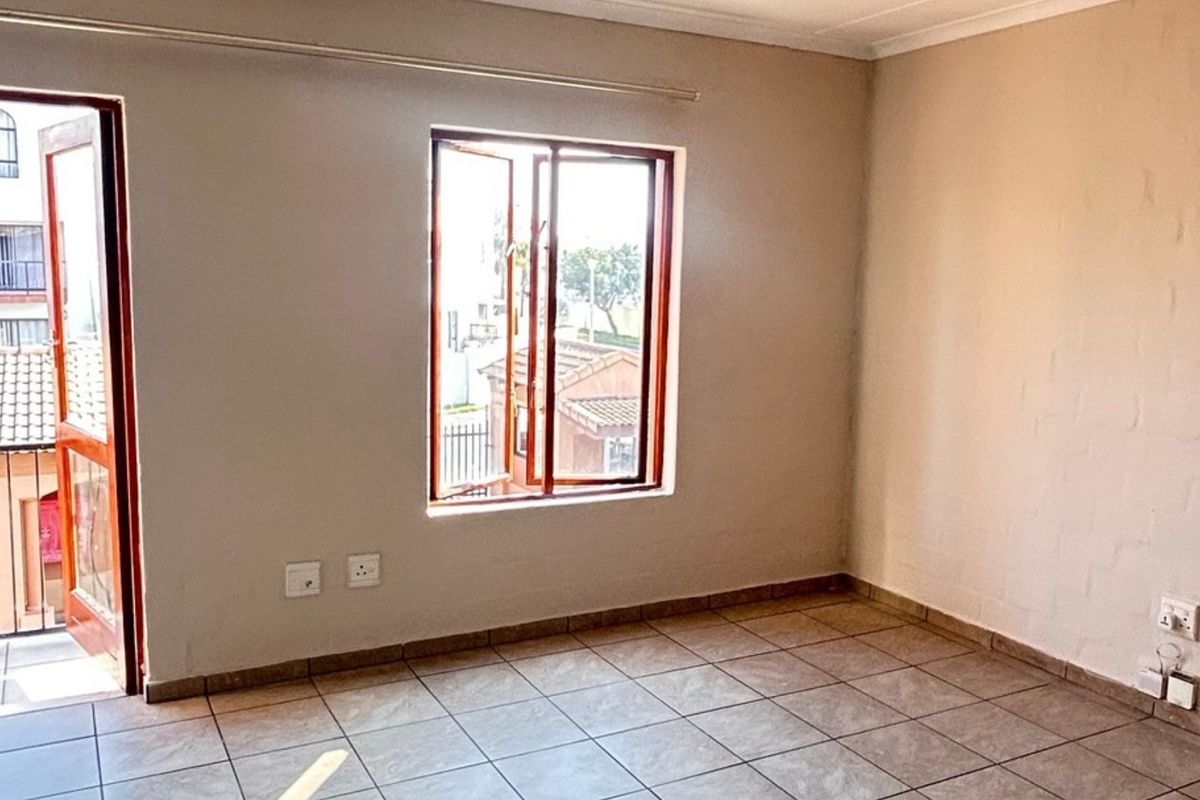 A bright, empty bedroom featuring tiled flooring, neutral walls, and a wooden window frame with access to an adjacent balcony.