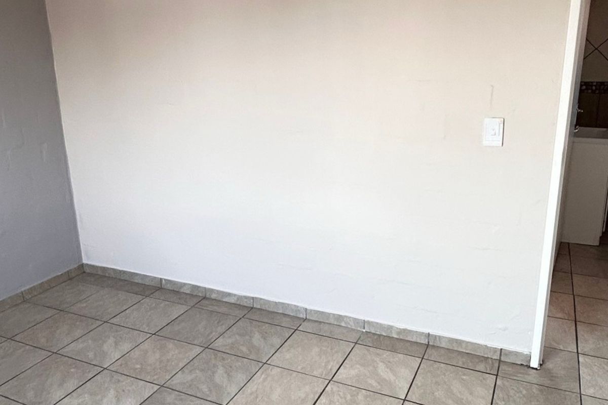 An empty living area featuring neutral painted walls and ceramic floor tiles with matching tiled skirting, providing a clean and versatile space.