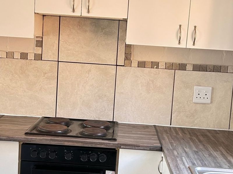 A functional kitchen area featuring white cabinetry, a dark laminate countertop, built-in electric oven and hob, and a tiled backsplash.