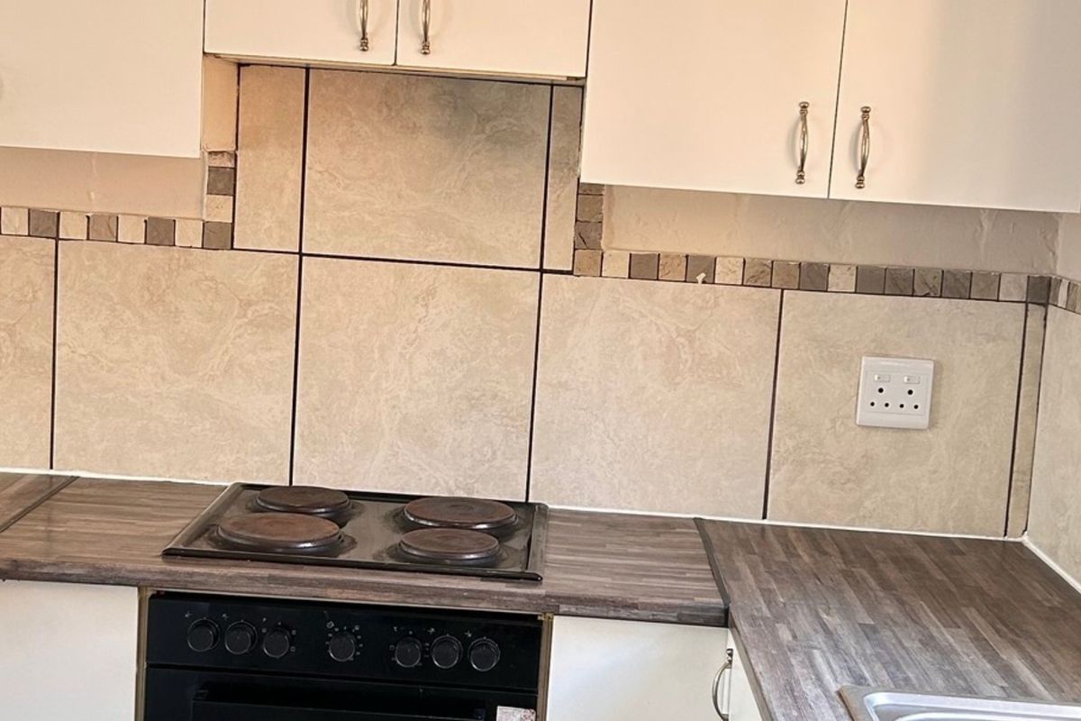 A functional kitchen area featuring white cabinetry, a dark laminate countertop, built-in electric oven and hob, and a tiled backsplash.